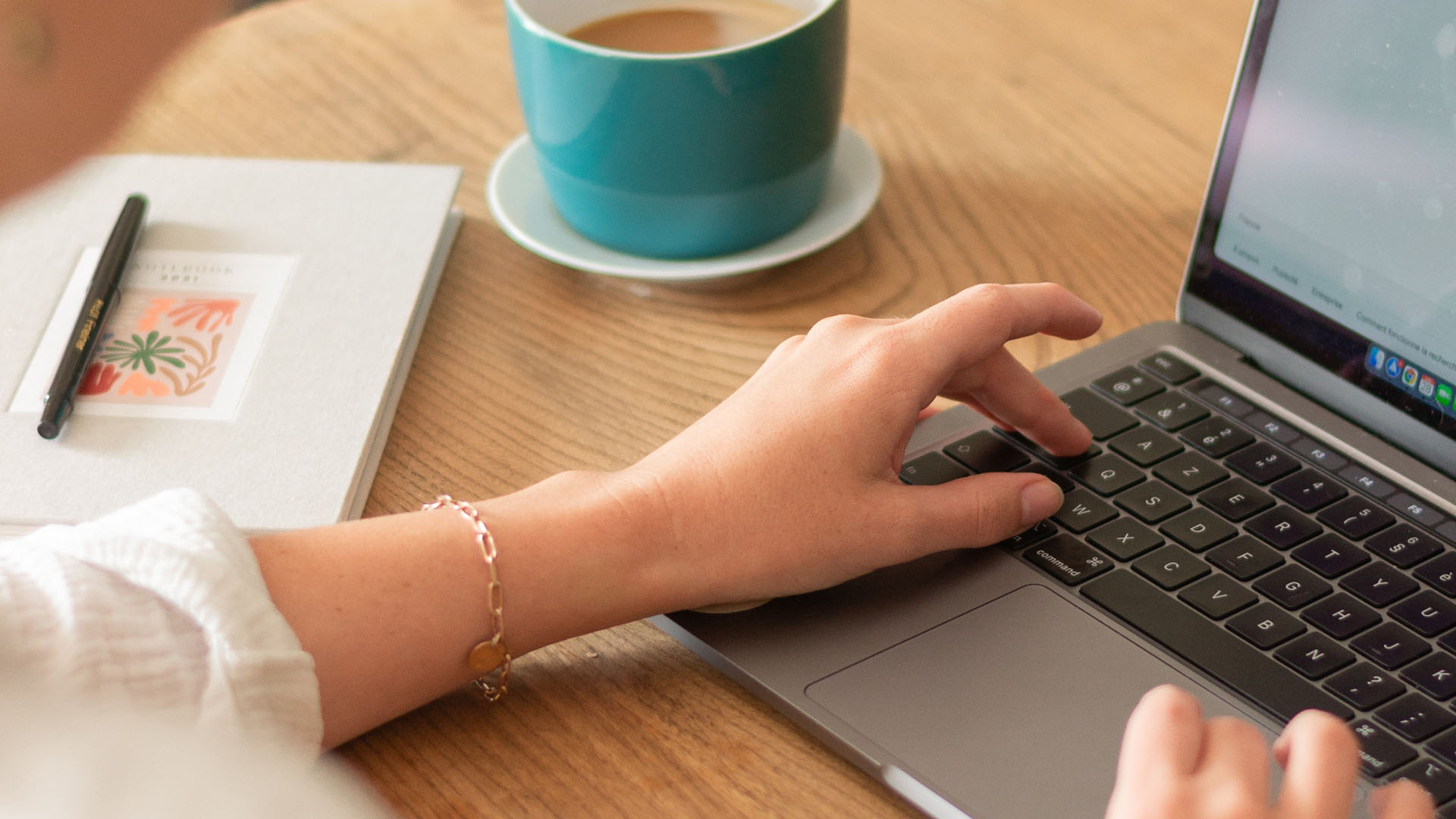 Person working at desk with coffee cup, journal with pen, and laptop computer.