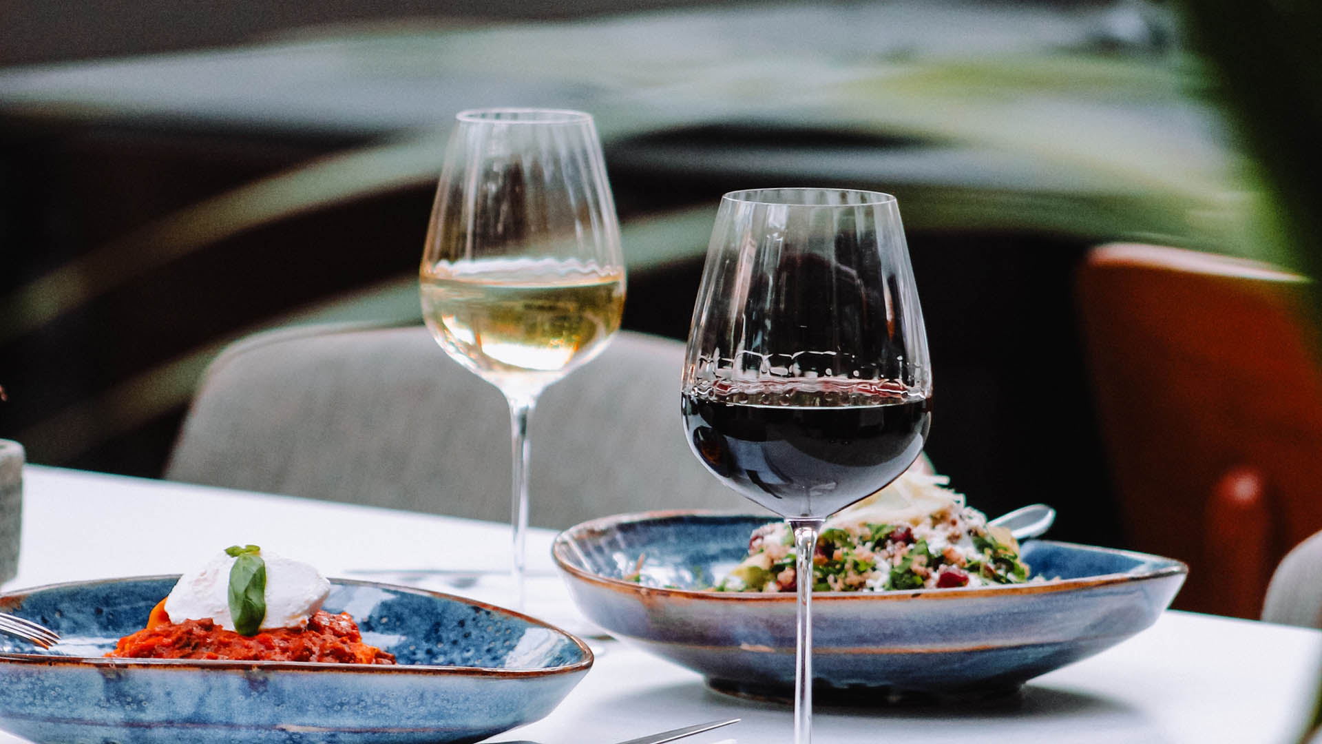 Dining table with elegant blue plates of food and tall wine glasses.