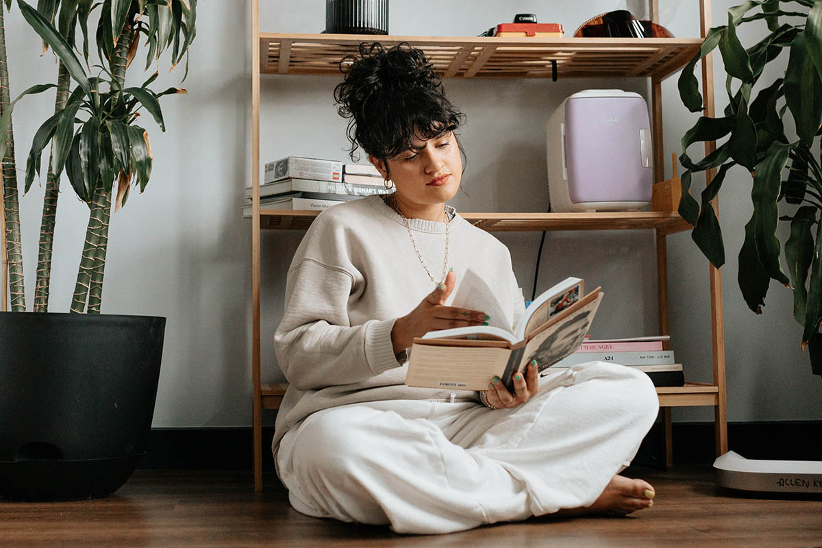 Person sitting and reading in front of bookshelf with books, cameras, and decor.