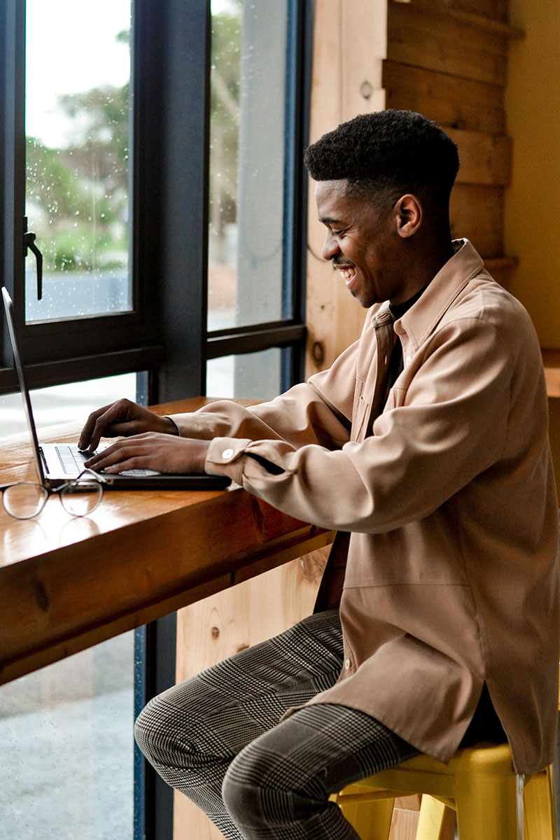 Person smiling while working on computer at coffee shop table.