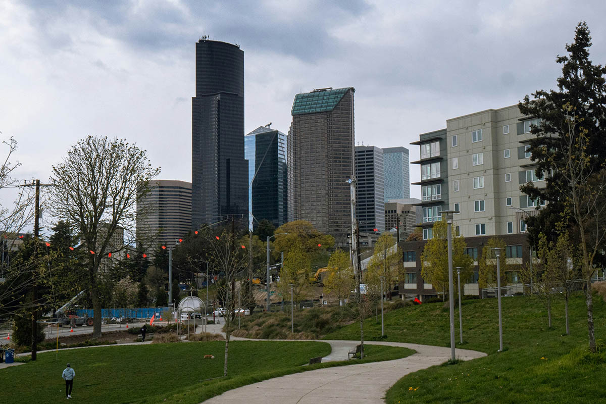 Yesler Terrace park with winding concrete paths, lush green lawns, and the Seattle skyline beyond.