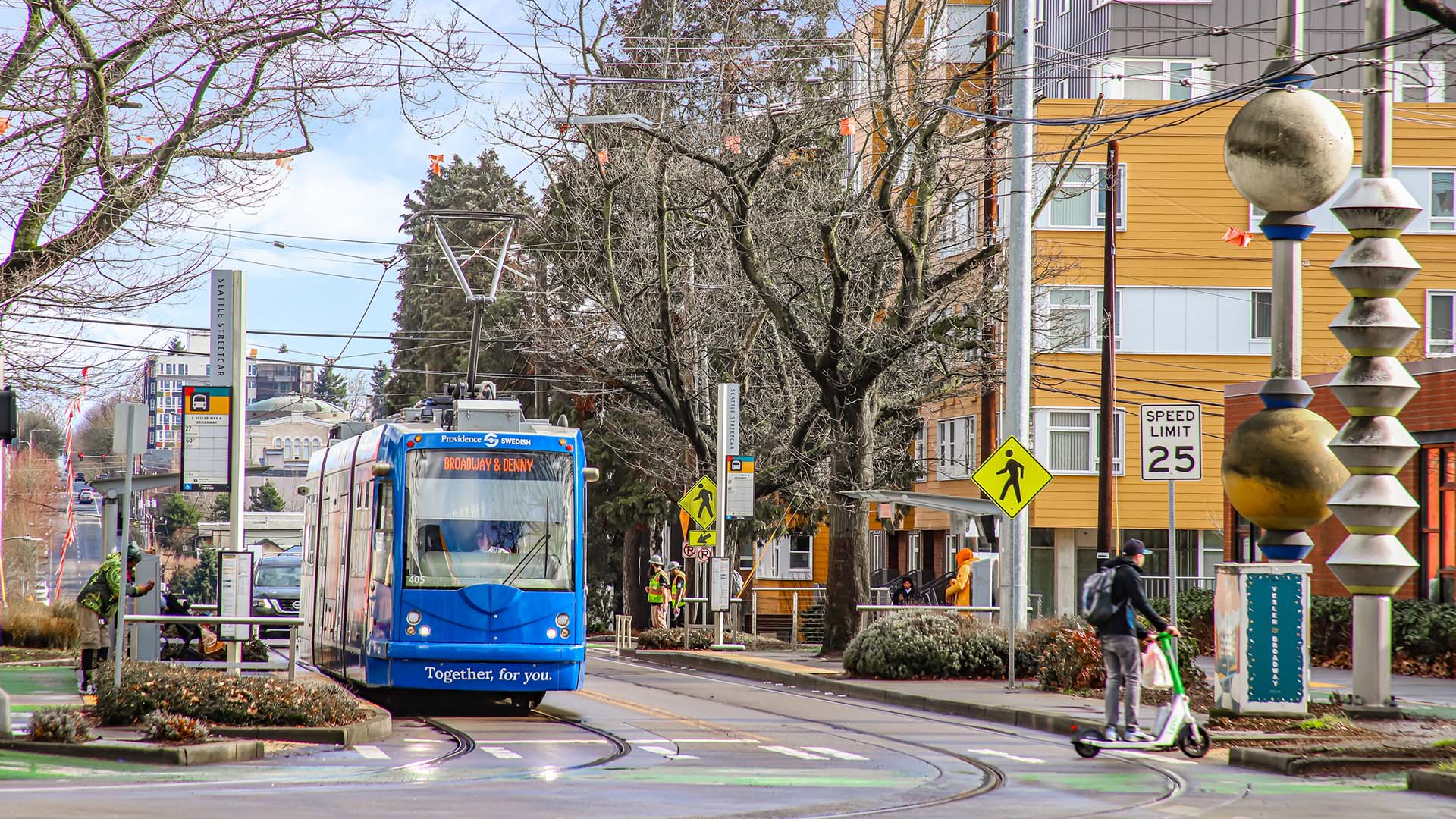 Seattle city street bustling with tall trees and interesting sculptures bustling with trains and pedestrians.